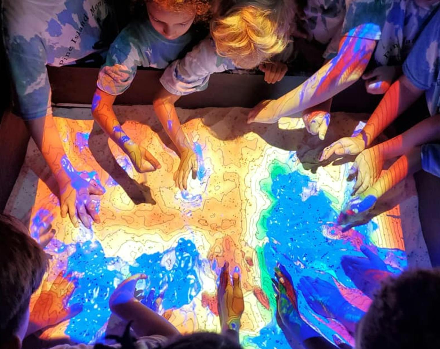 People interacting with a colorful, illuminated topographic map
