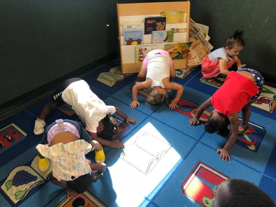 Children doing yoga poses on a blue rug in a classroom