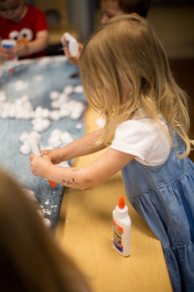 Child in a classroom doing an art project with cotton balls and glue