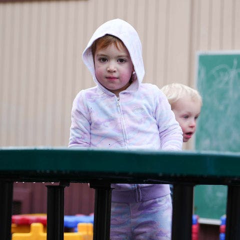 Child in a hoodie behind a railing with another child in the background