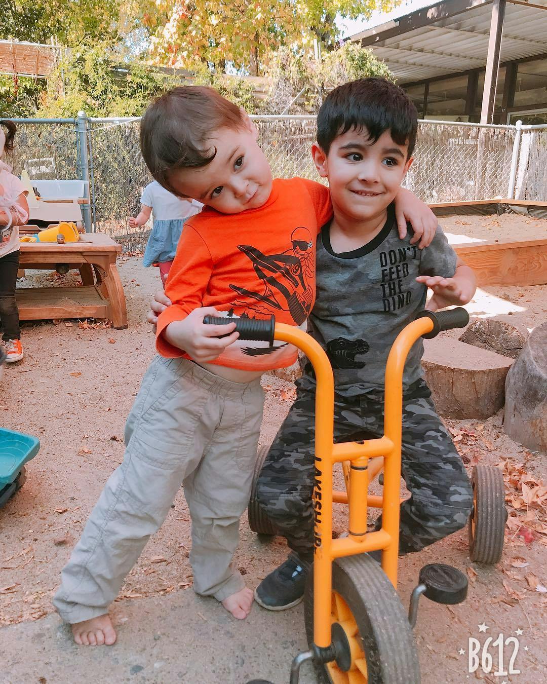 Two children standing next to a tricycle