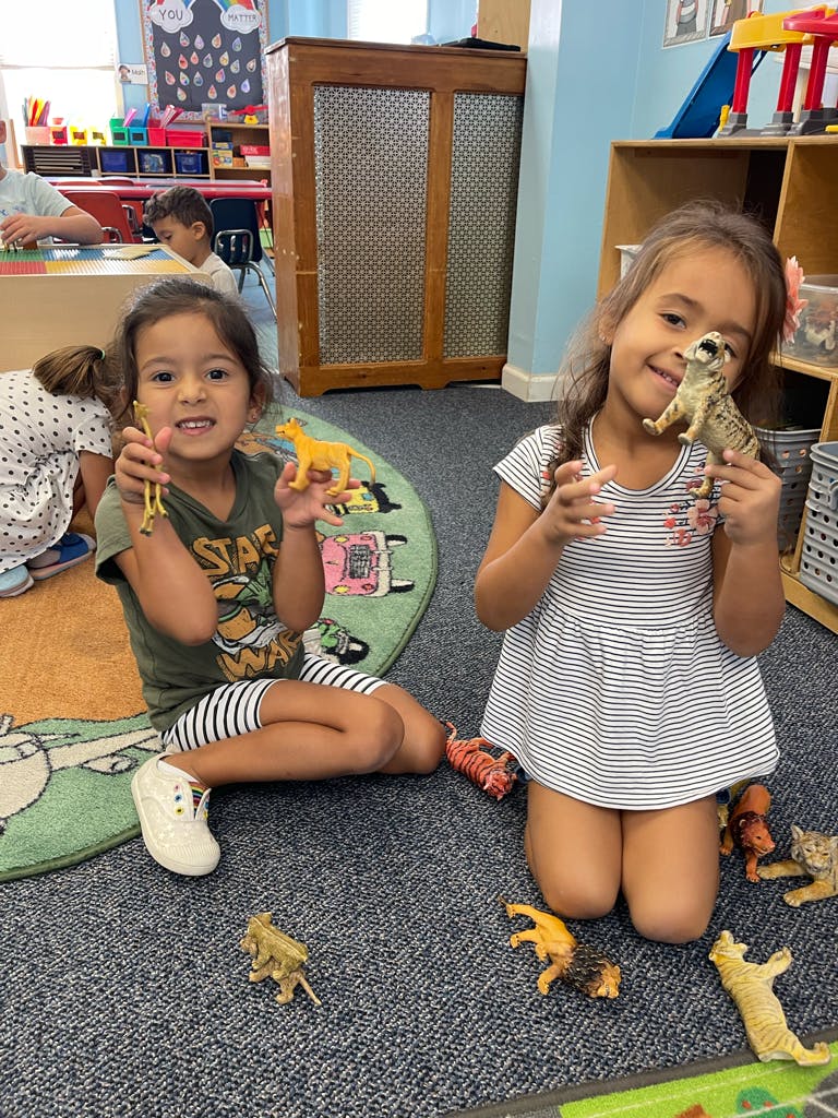 Two children sitting on a rug holding toy animals