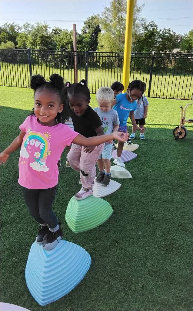 Children balancing on colorful stepping stones on a grassy surface