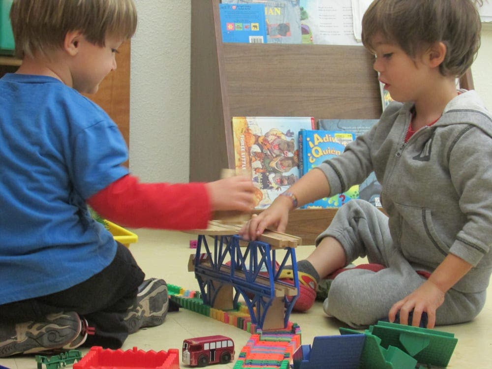 Two children playing with building blocks and toy vehicles on the floor