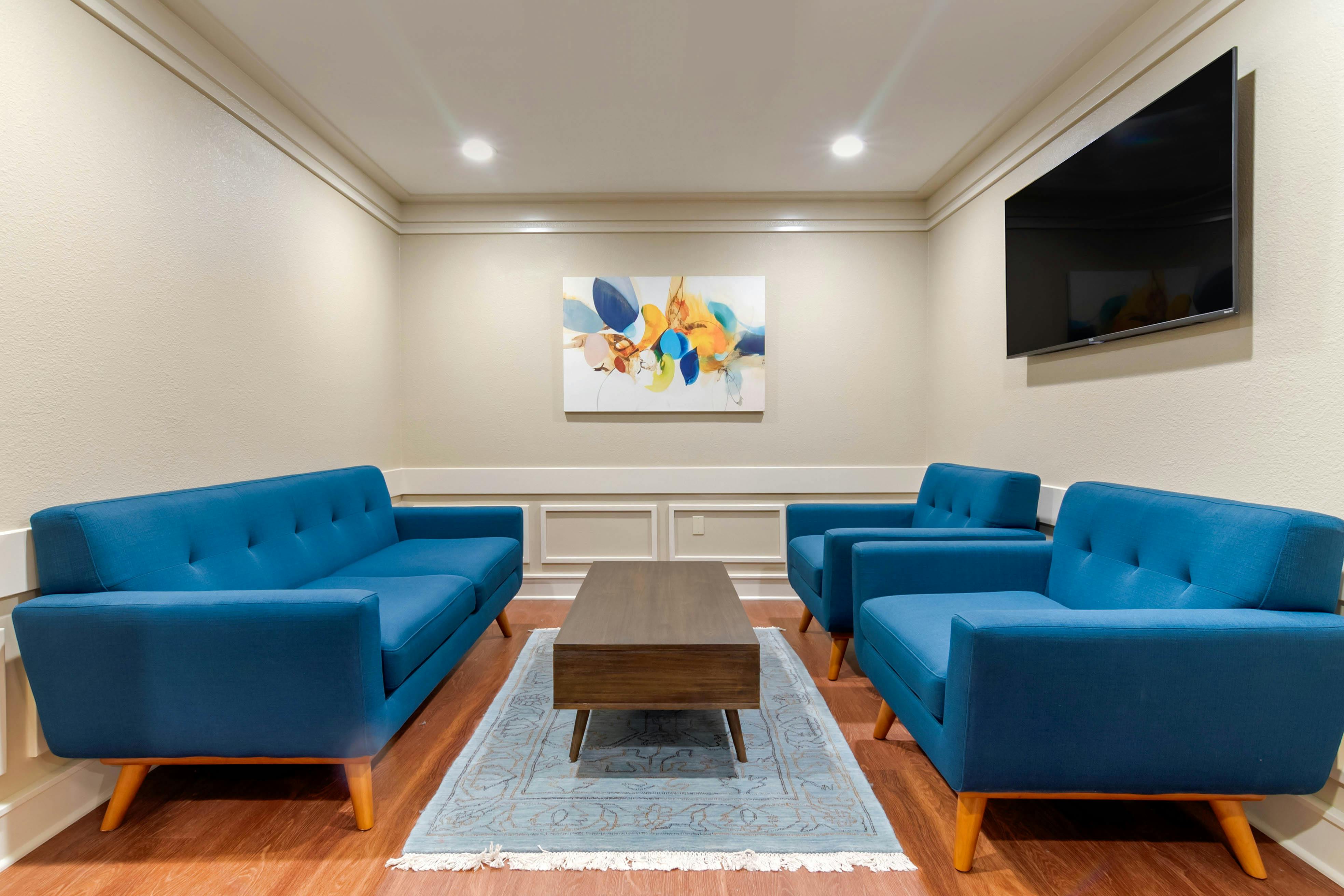 A room with blue sofas, a coffee table, abstract art, and a wall-mounted TV