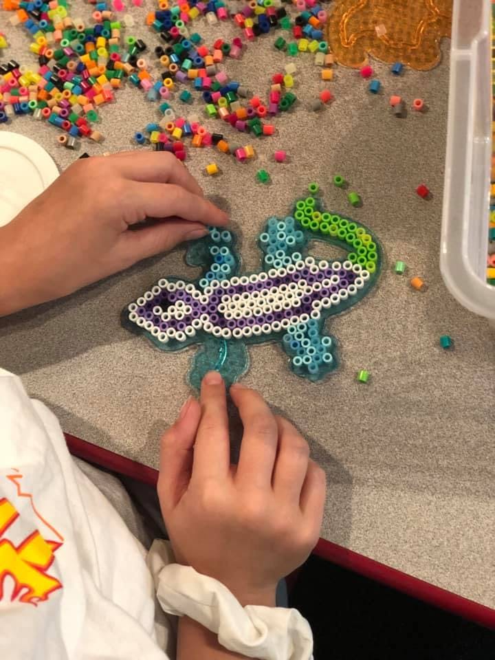Person's hands working on a lizard-shaped perler bead craft
