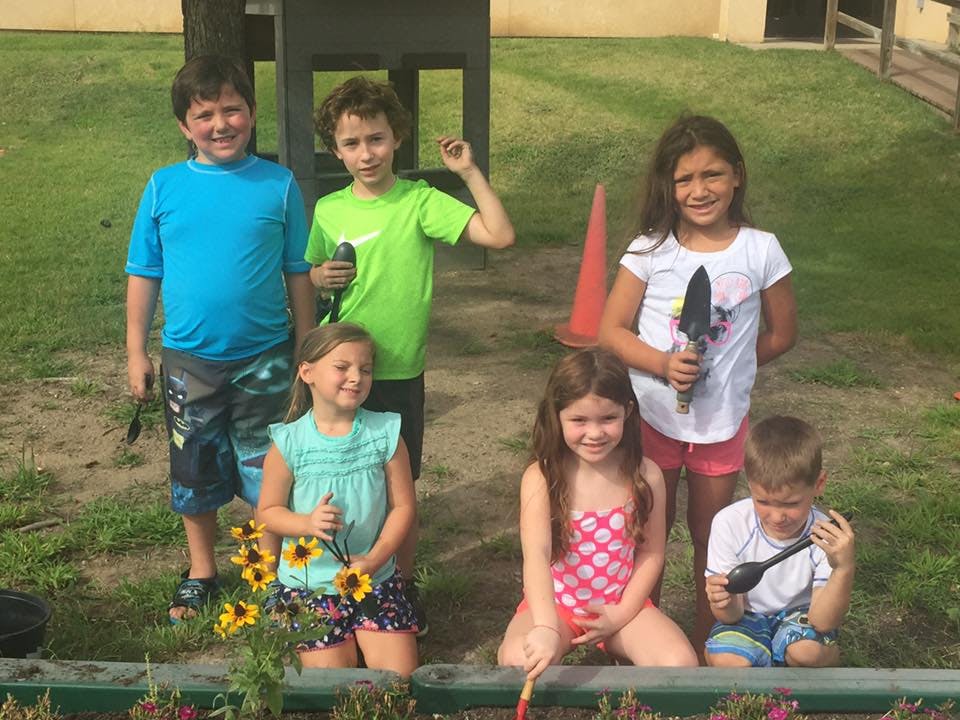 Group of children holding gardening tools and flowers outdoors