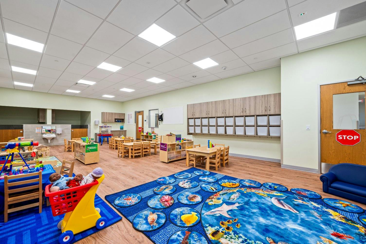 A classroom with small tables and chairs, a play area, and cubbies