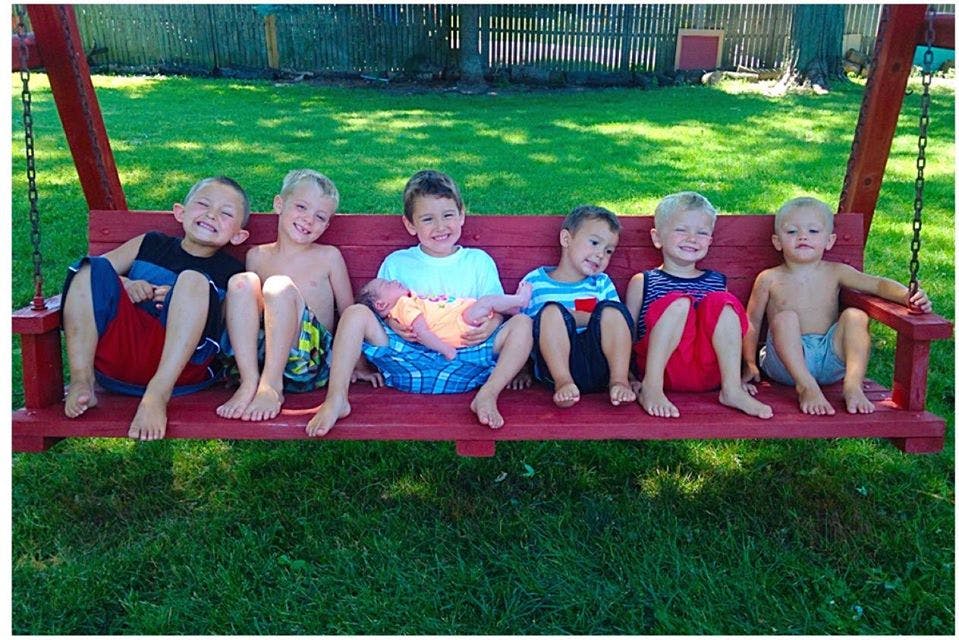 Six children sitting on a red porch swing