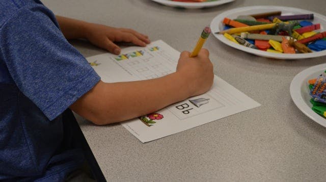 Child writing on paper with a pencil