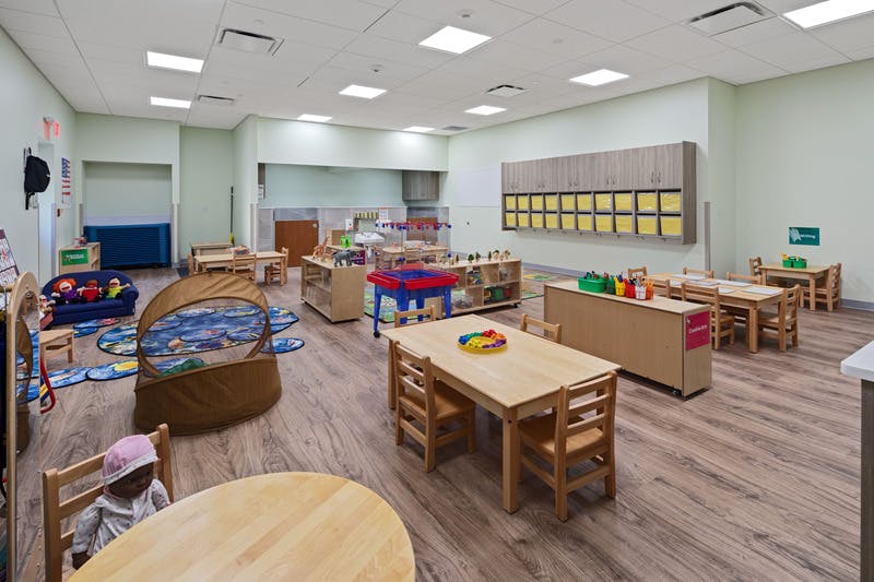A colorful empty classroom with small tables, chairs, and play areas