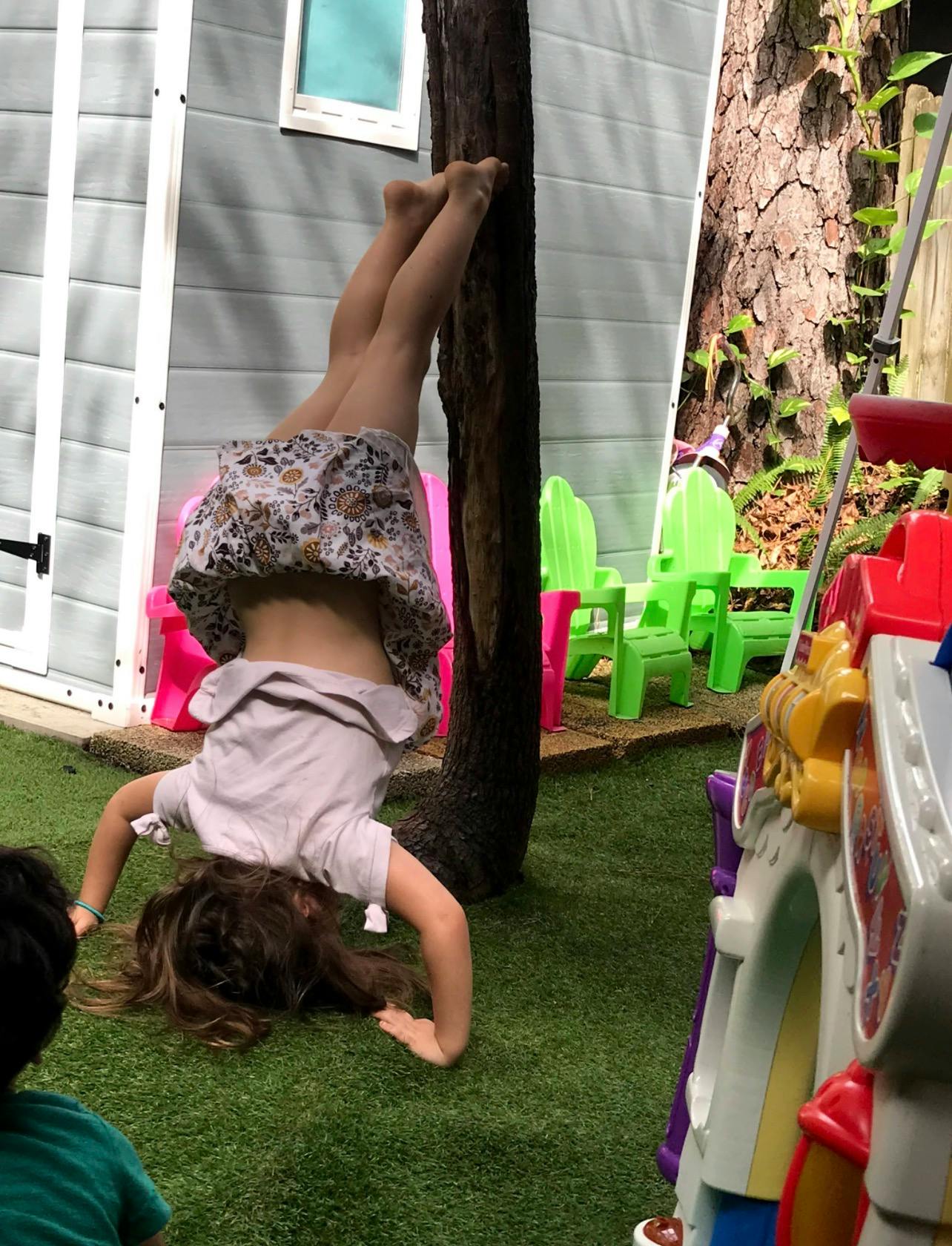 Child doing a handstand against a tree in a yard