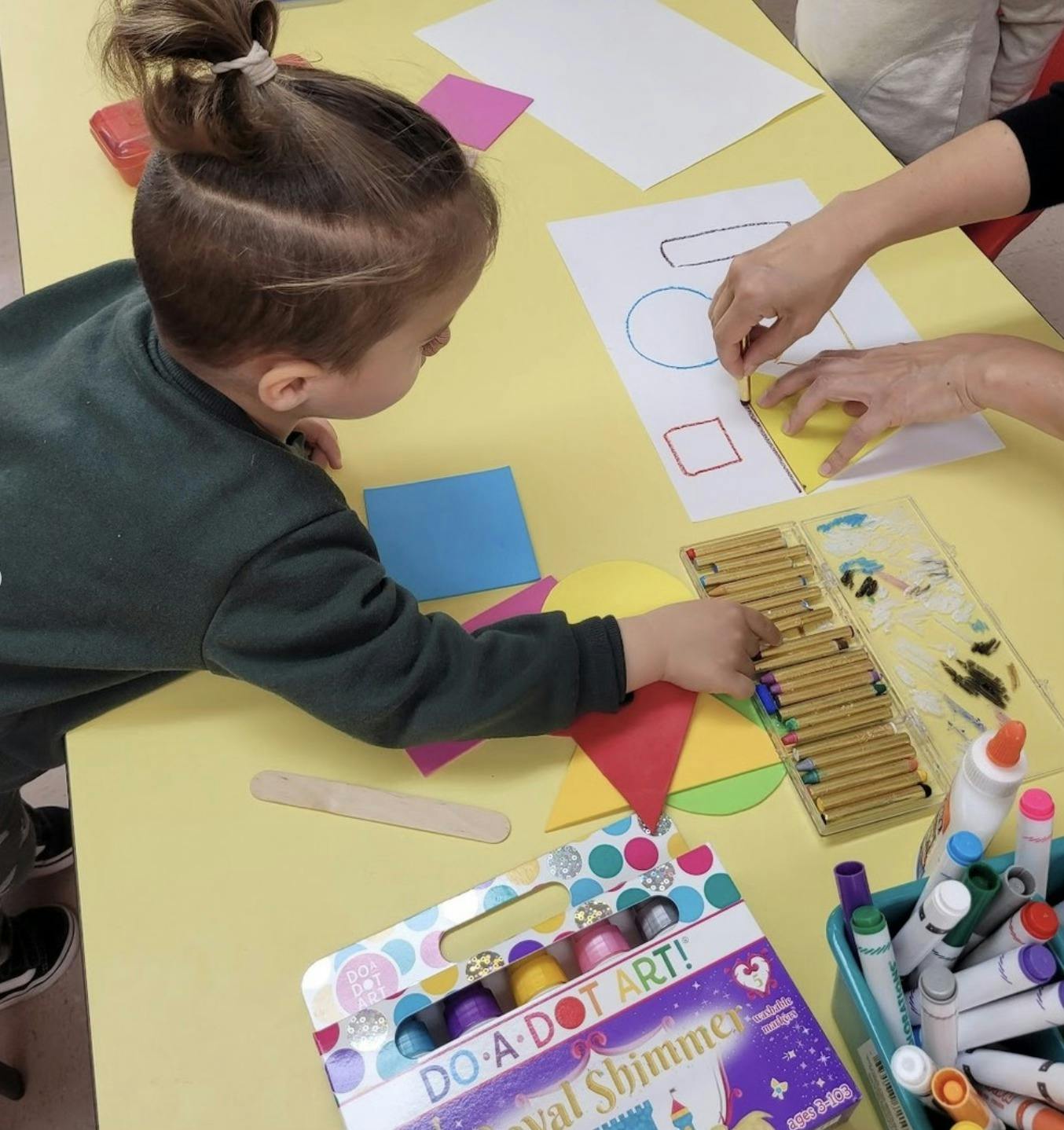 Child and person drawing shapes at a table