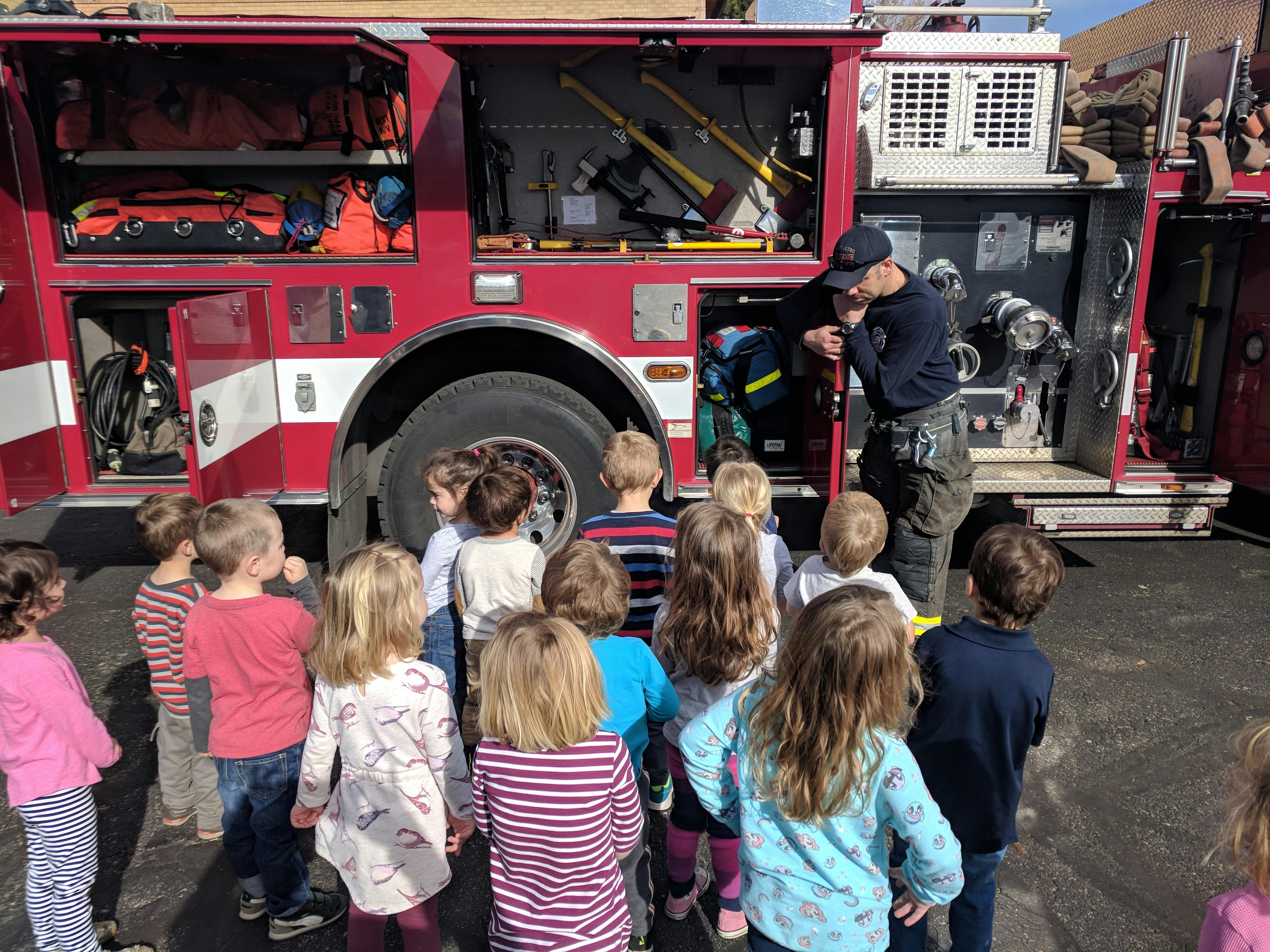Firefighter showing equipment on a fire truck to a group of children