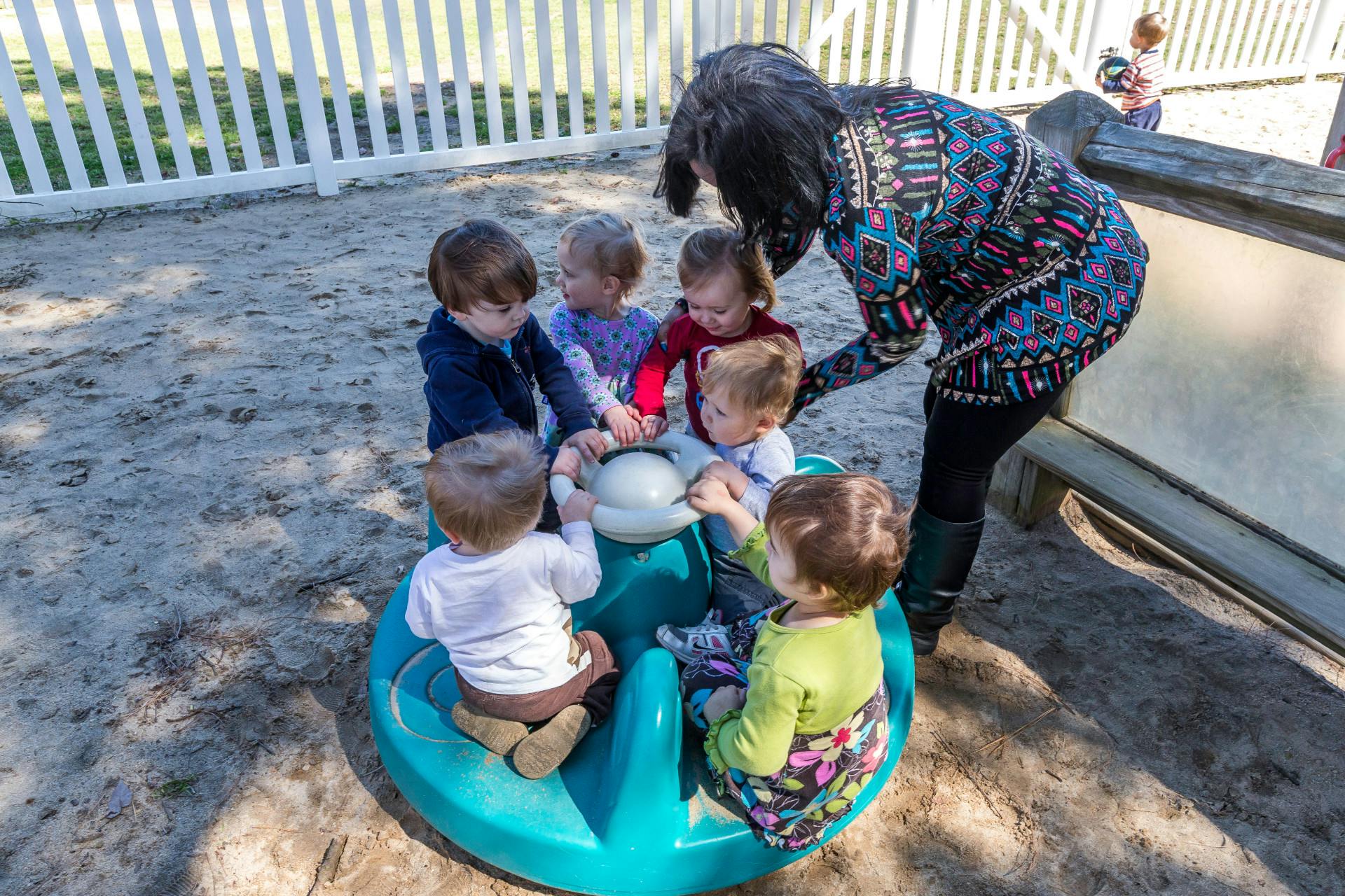 Adult helping children on a playground merry-go-round