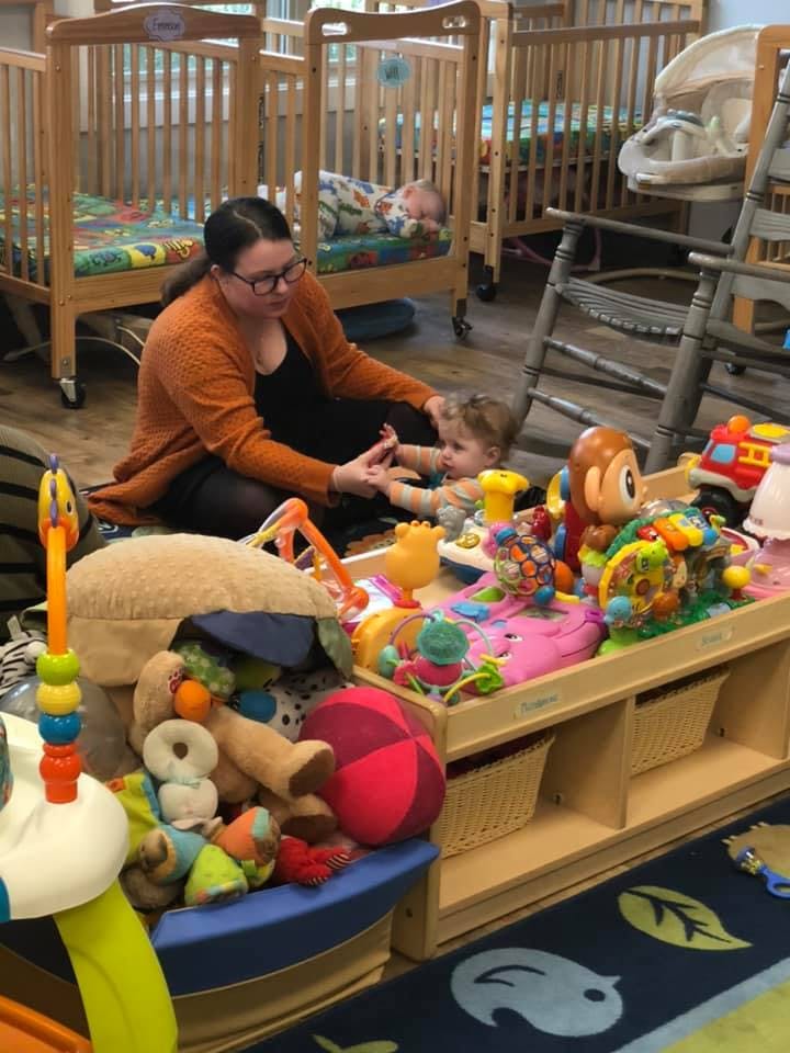 Person sitting on floor playing with a child surrounded by toys