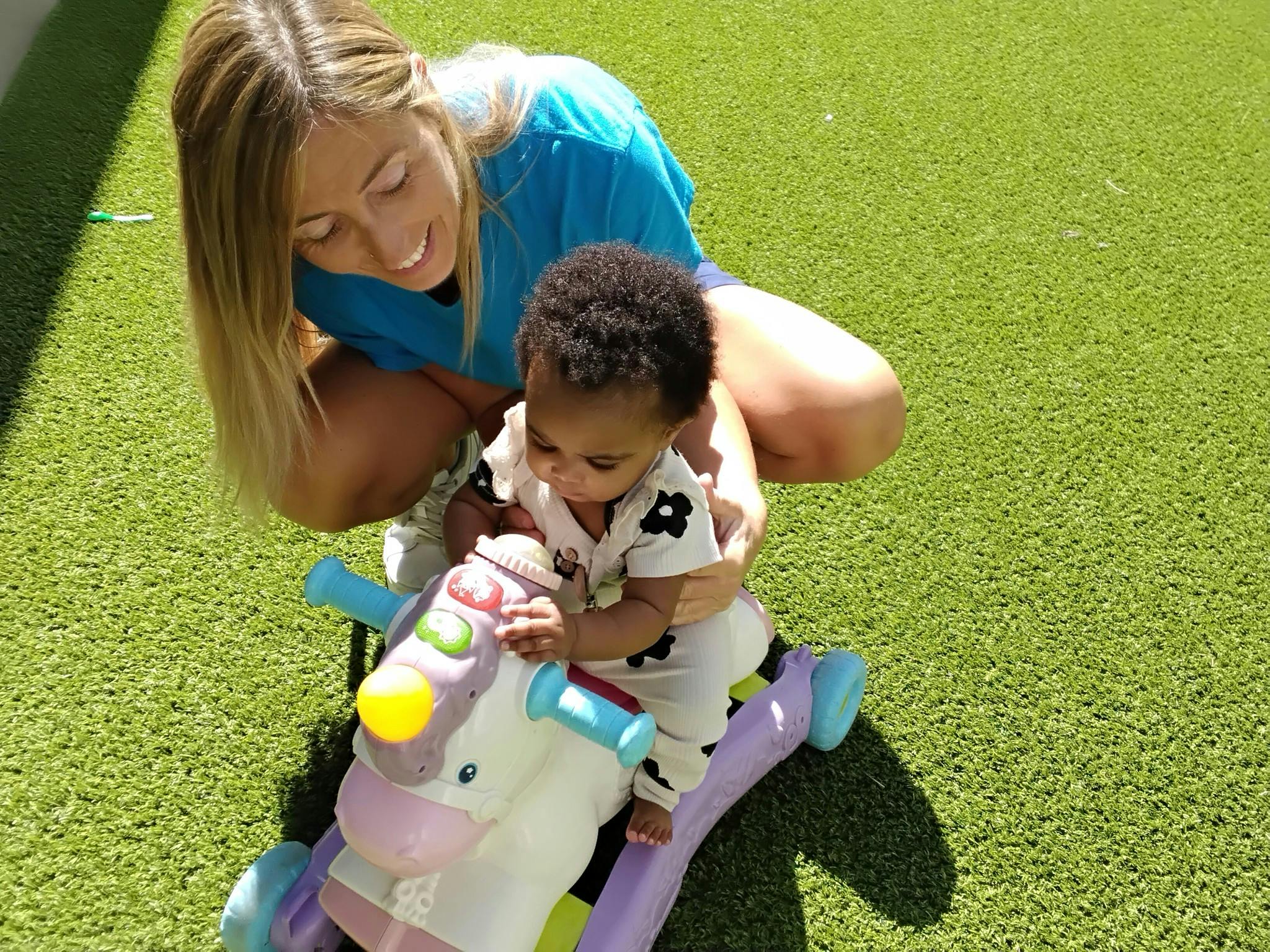 Adult person crouching with a child on a ride-on toy on artificial grass