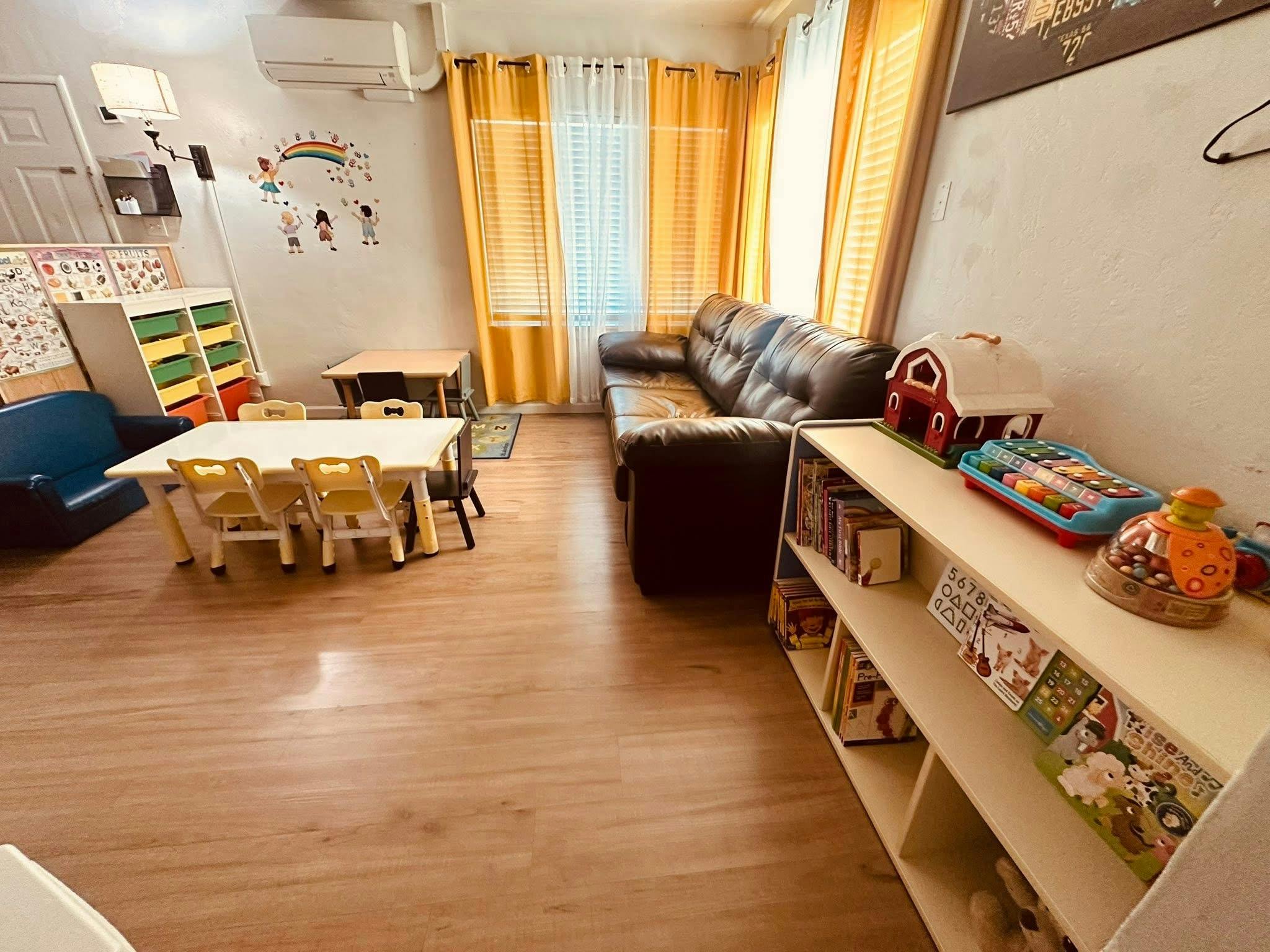 A classroom with small tables and chairs, a couch, and shelves with books and toys