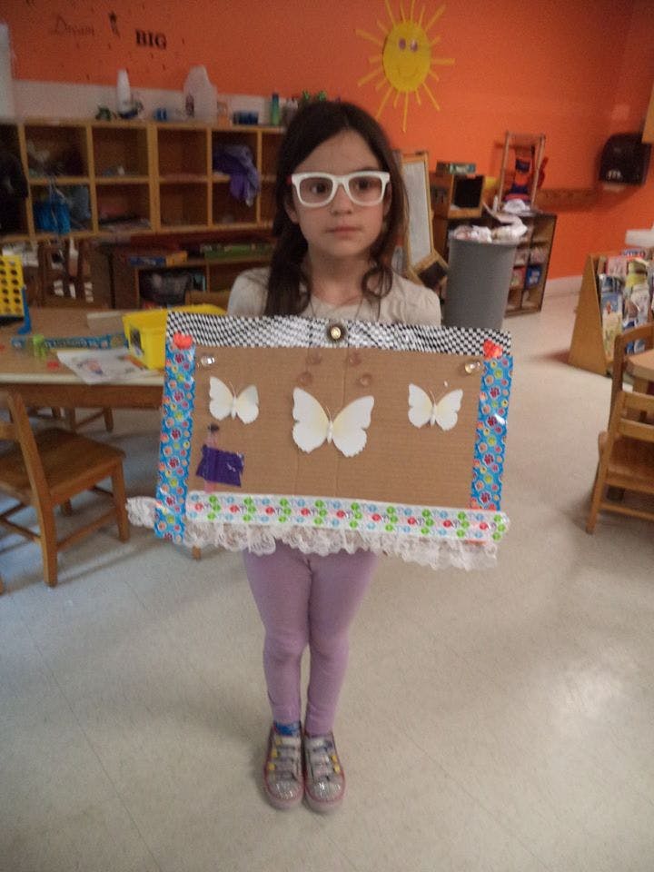 Child wearing glasses holding a decorated cardboard sign with butterflies