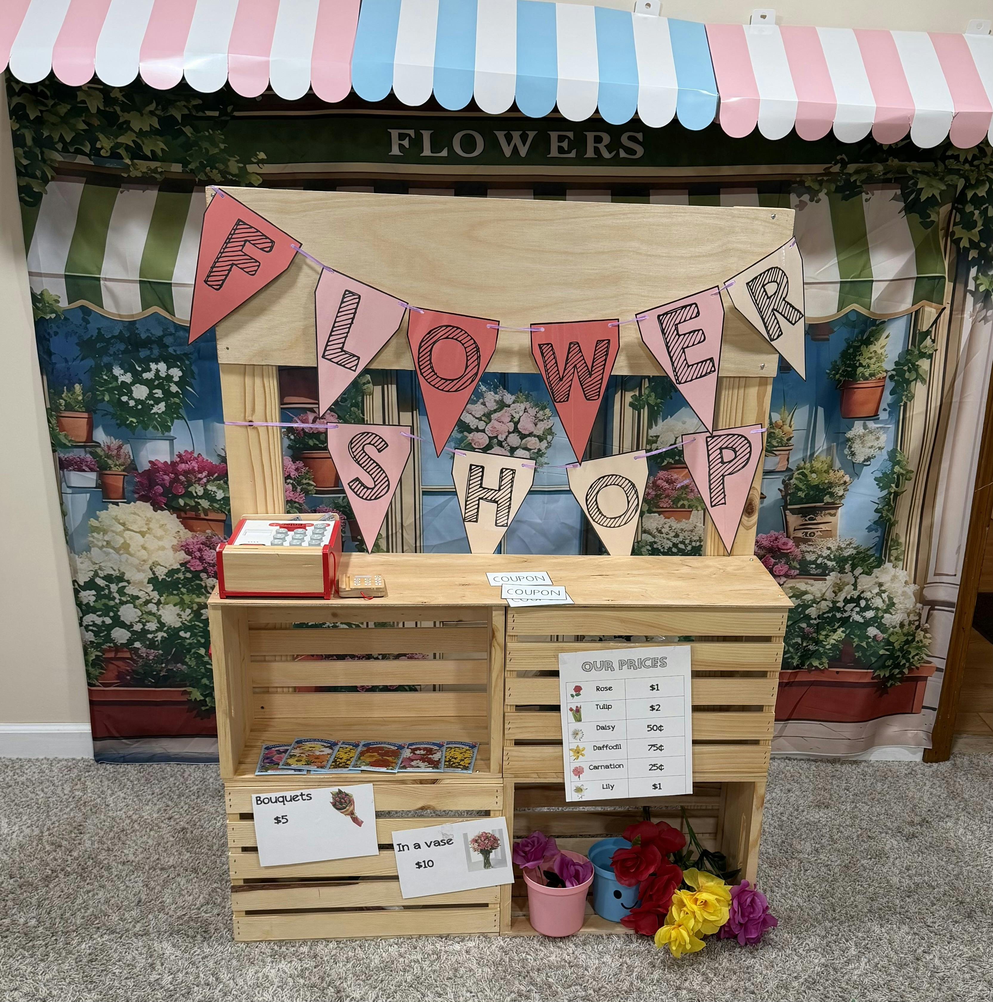 A wooden flower shop play stand with a price list and paper banners