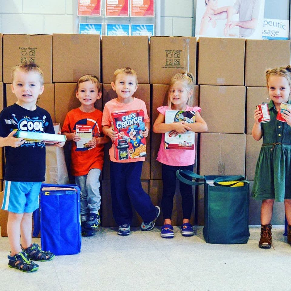 Five children standing in front of stacked boxes, holding various items
