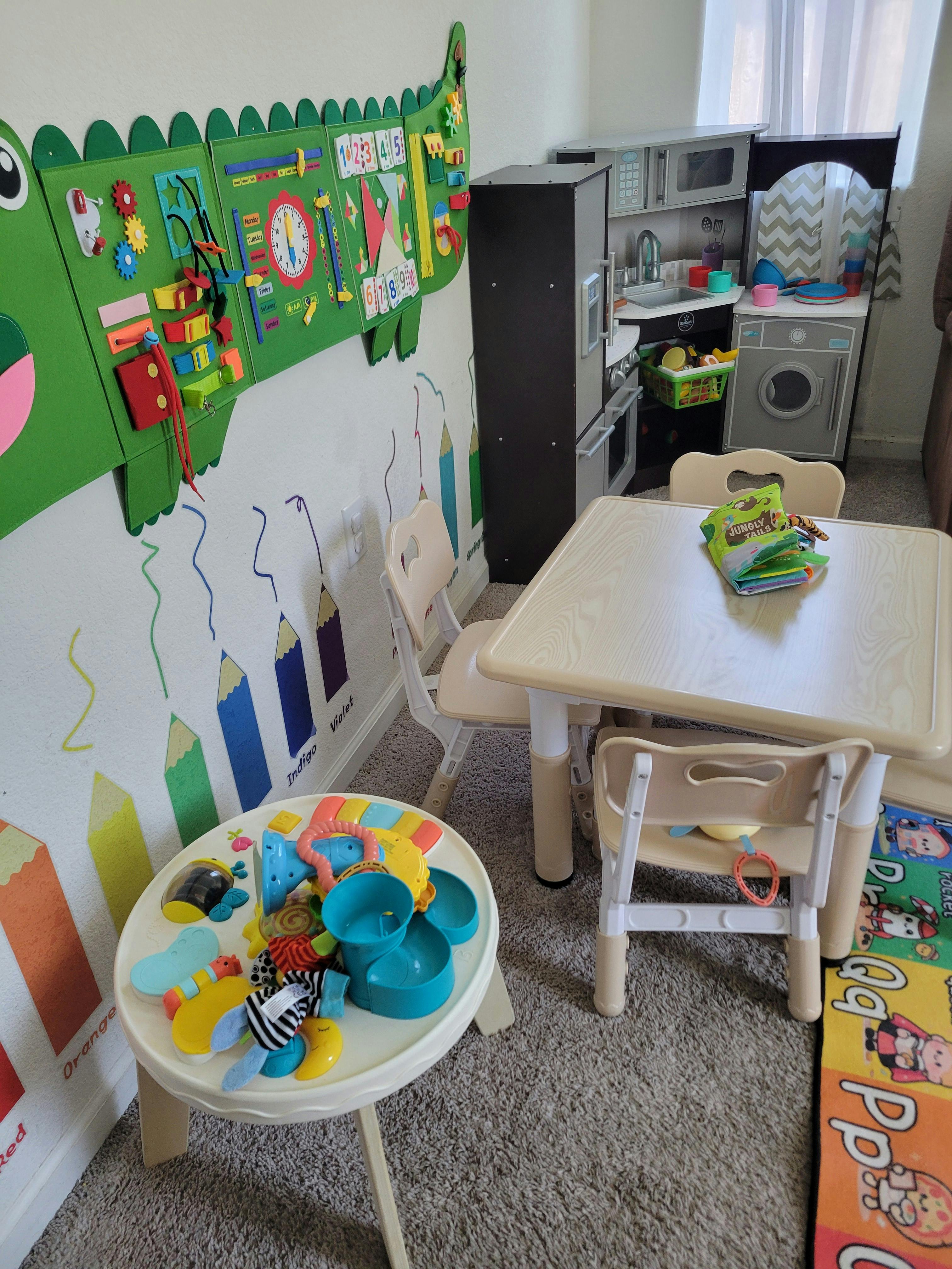 Child playroom with small table, play kitchen, and sensory wall activity board