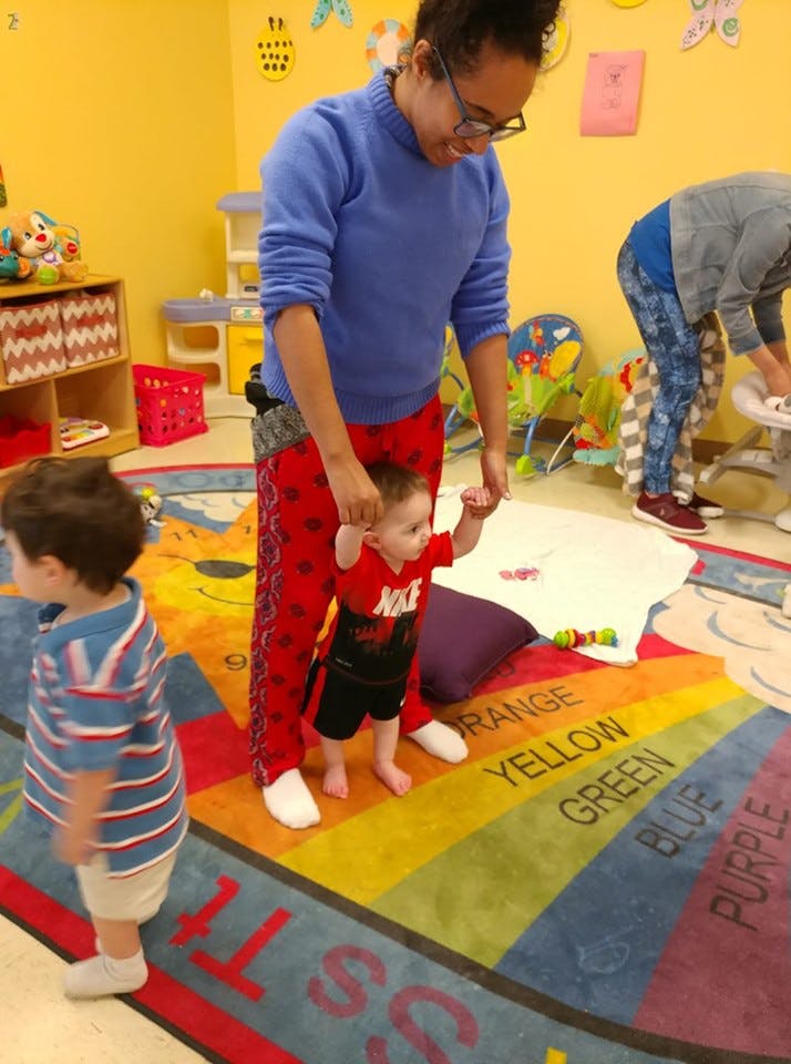 Person holding a child's hands to help them stand on a colorful rug