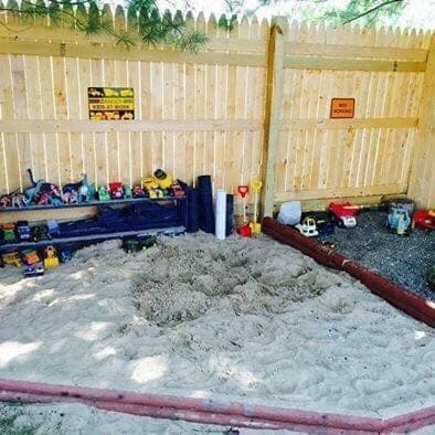 Outdoor sandbox with toys and a wooden fence