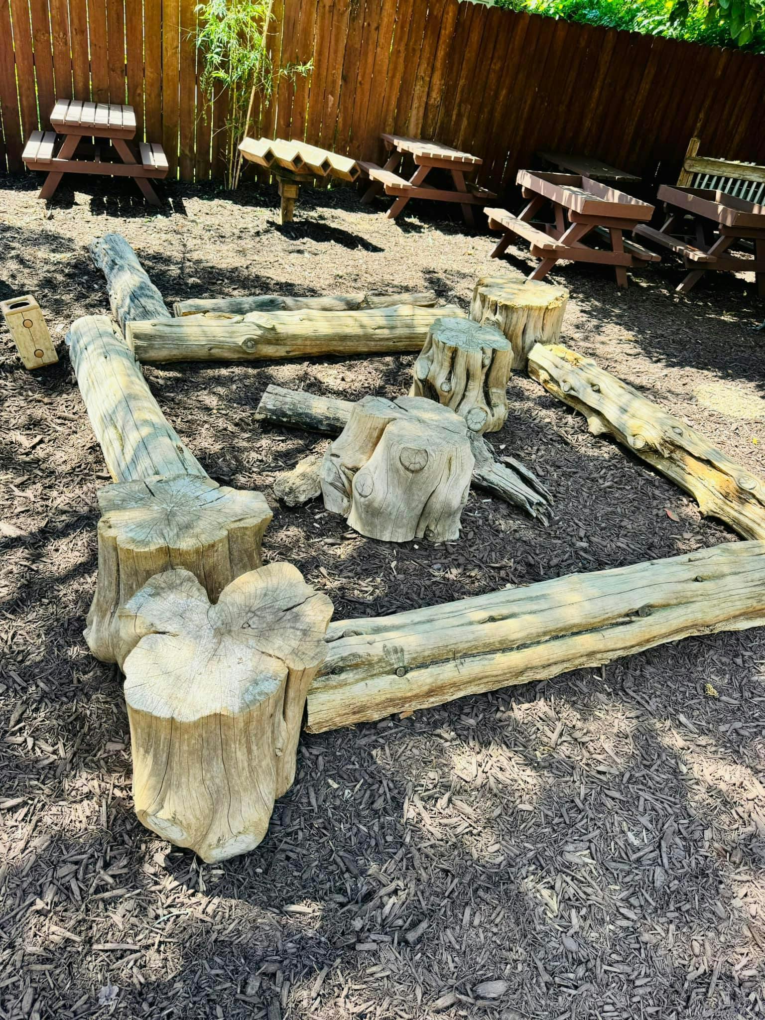 Logs and tree stumps arranged on wood chips with picnic tables in background