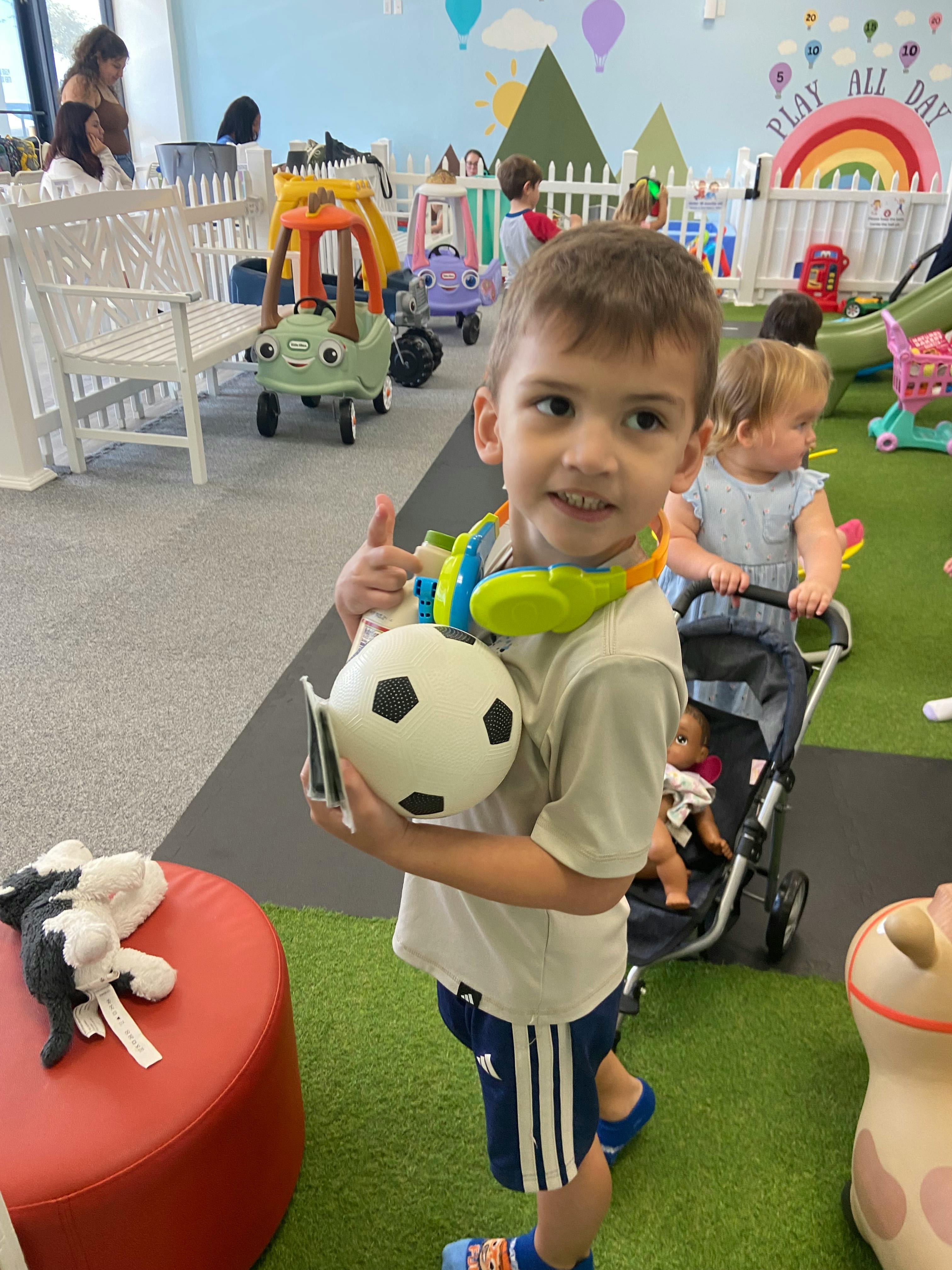 Child smiling, holding a soccer ball and cards in a play area