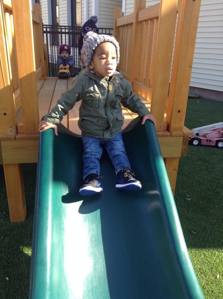 Child in a knit hat and jacket sitting at the top of a slide