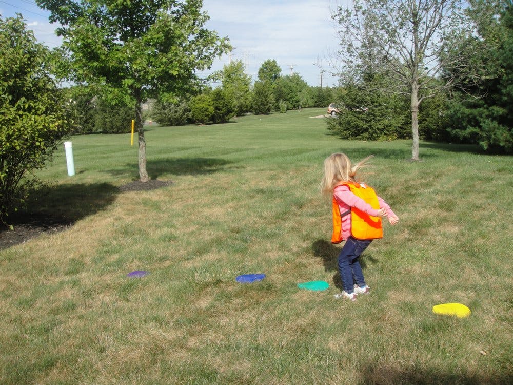 Child in an orange vest playing on a grassy field
