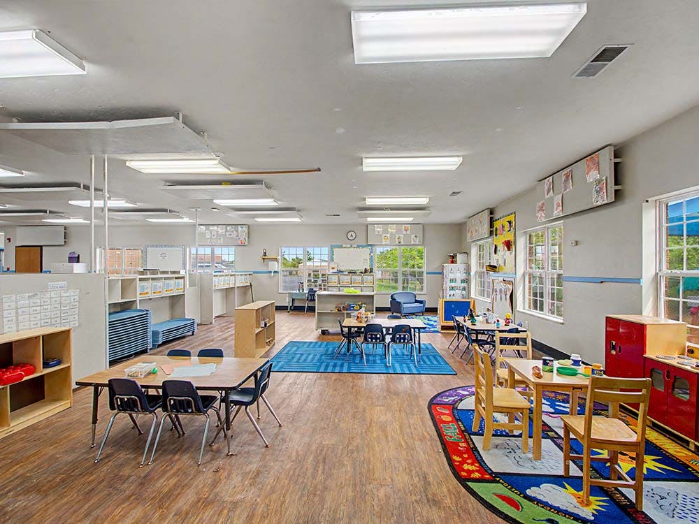 Empty classroom with small tables and chairs, and bright windows