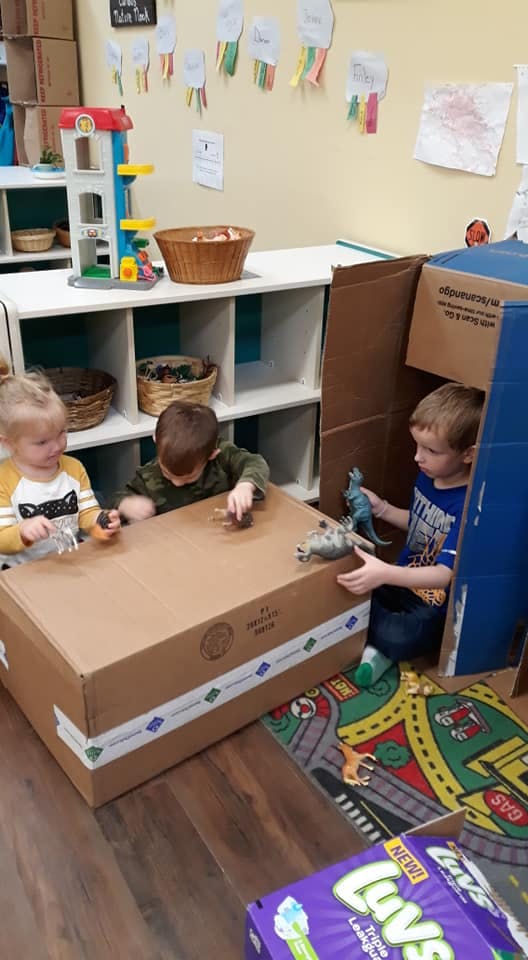 Three children playing with toys and cardboard boxes
