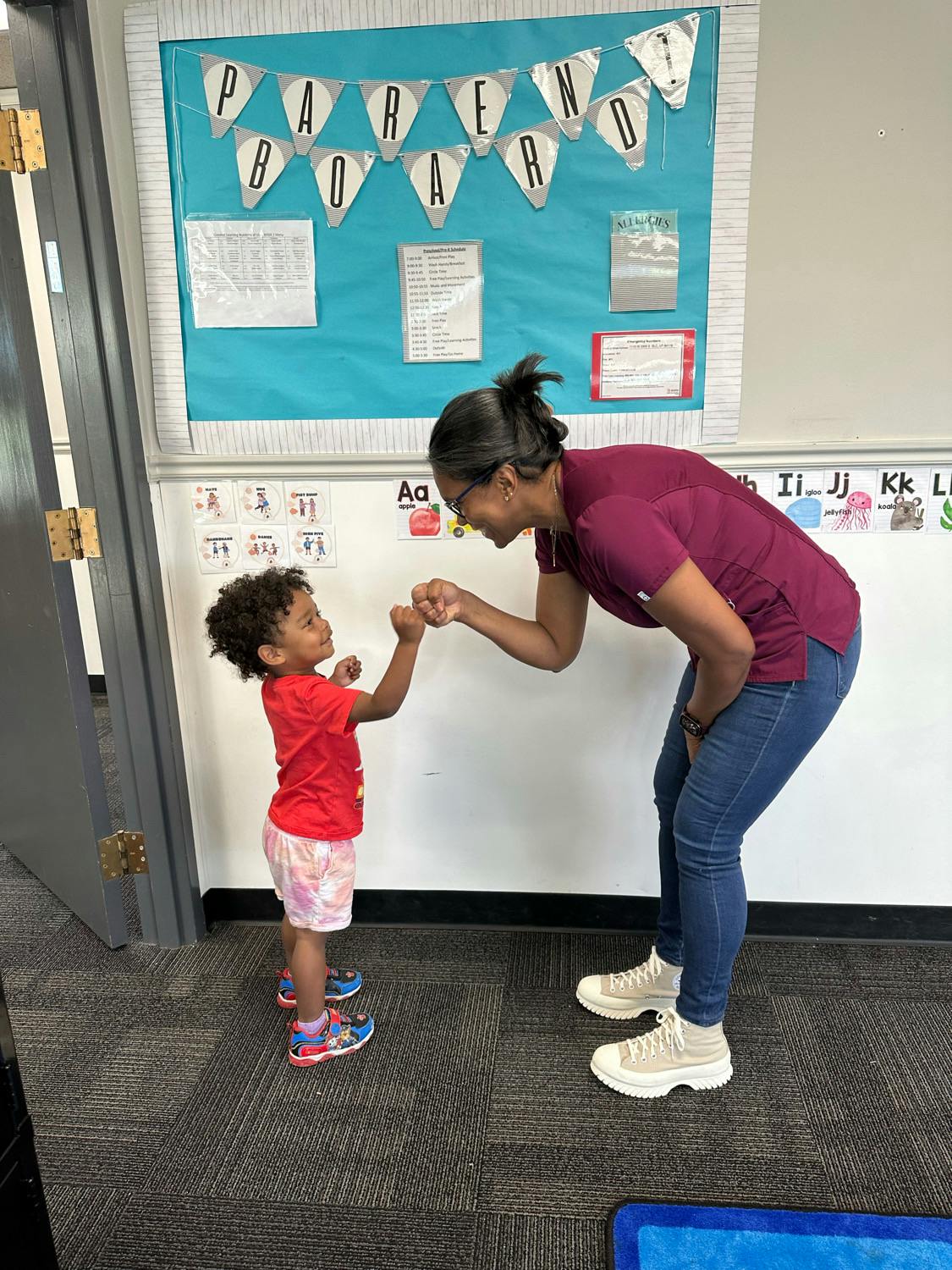 Adult and child doing a fist bump in a classroom