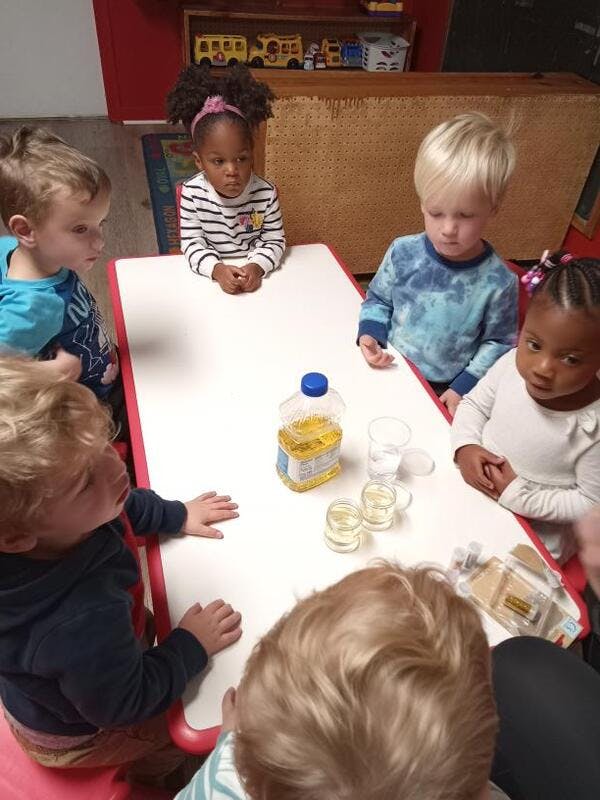 Children sitting around a table with a bottle of oil and small glasses