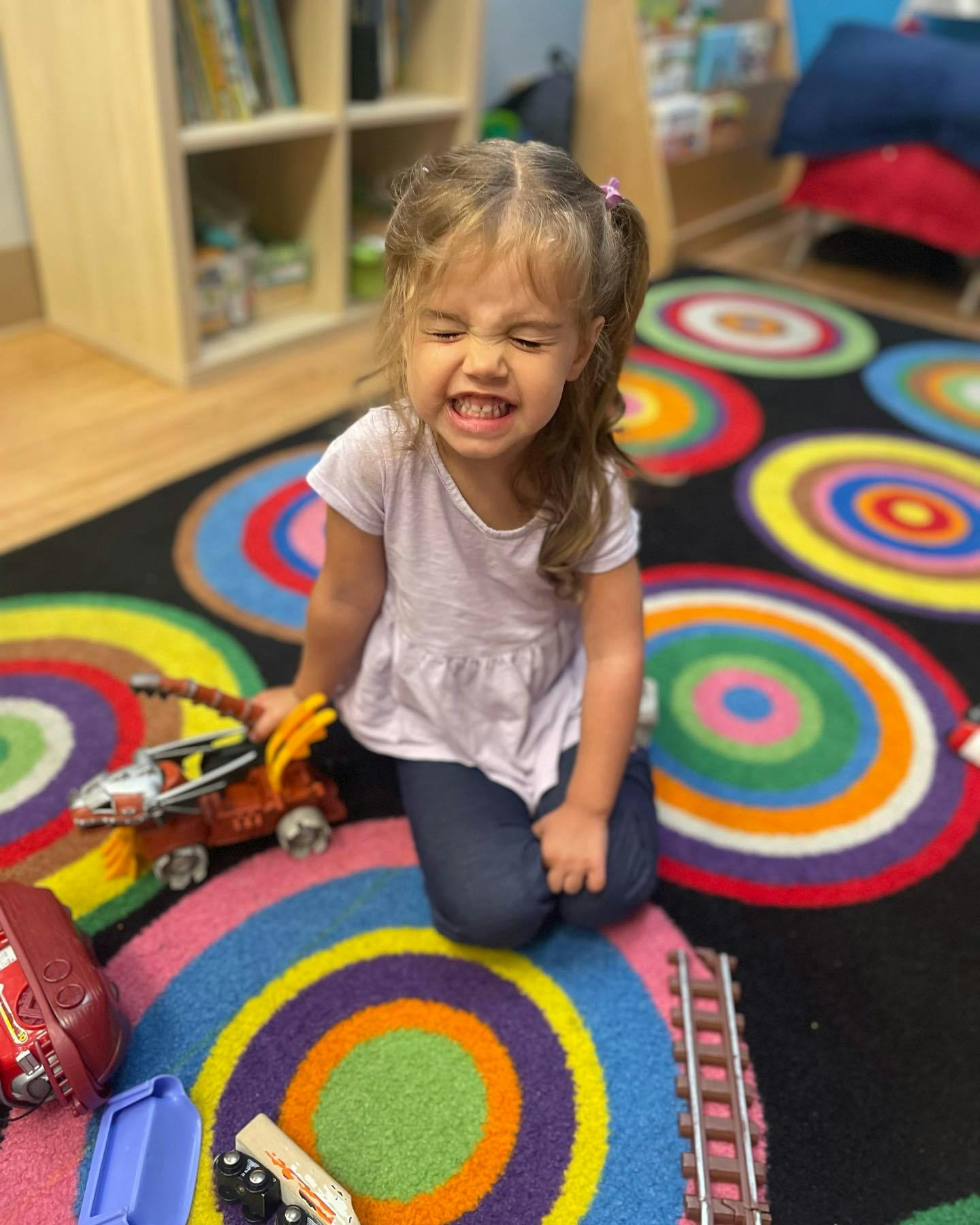 Child kneeling on a colorful rug with toys
