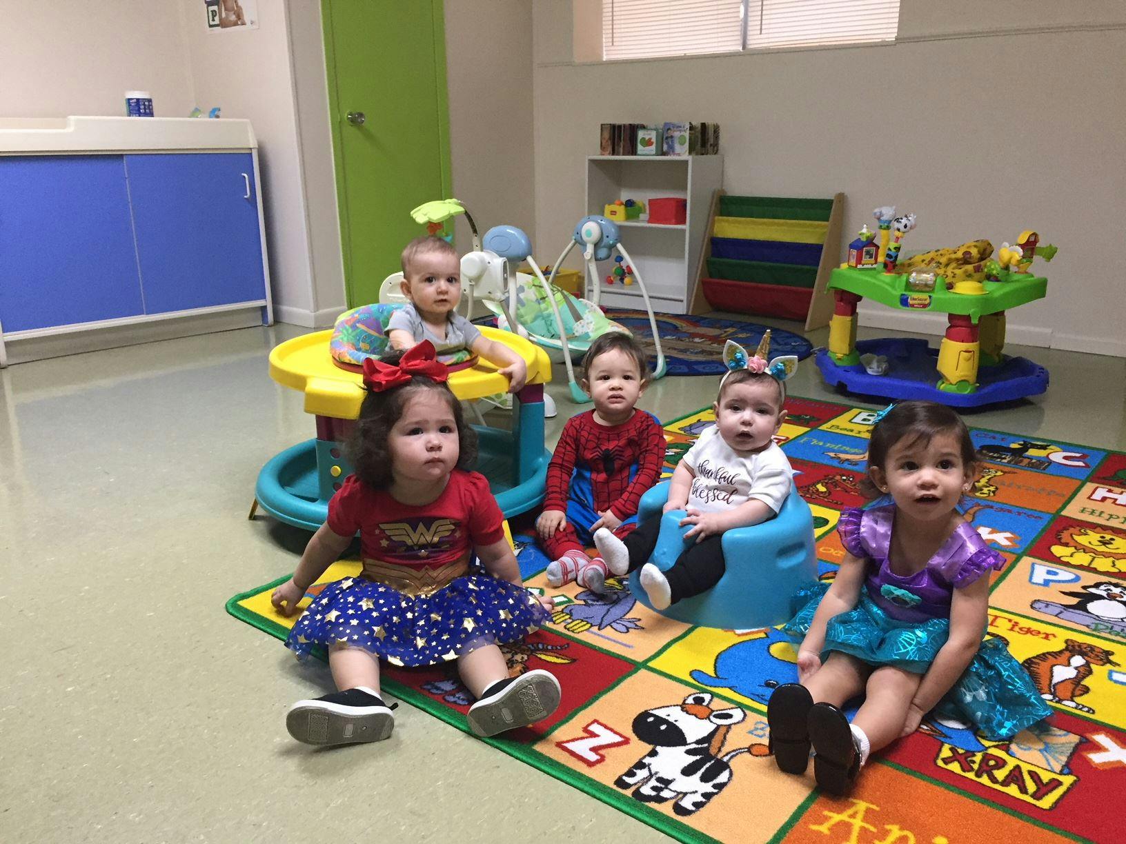 Five children sitting on a colorful playmat in a room with toys