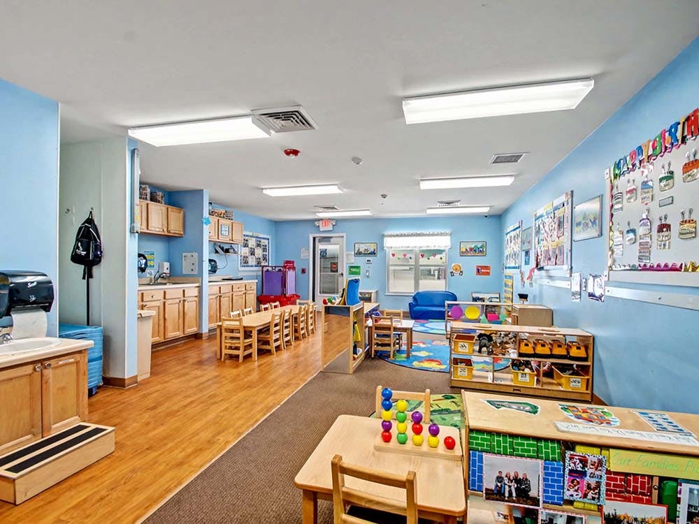 Classroom with tables, chairs, toys, and art on light blue walls