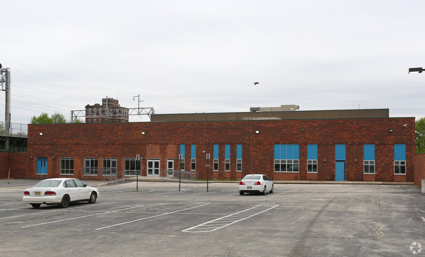 Brick building with blue windows and doors, and a parking lot with cars