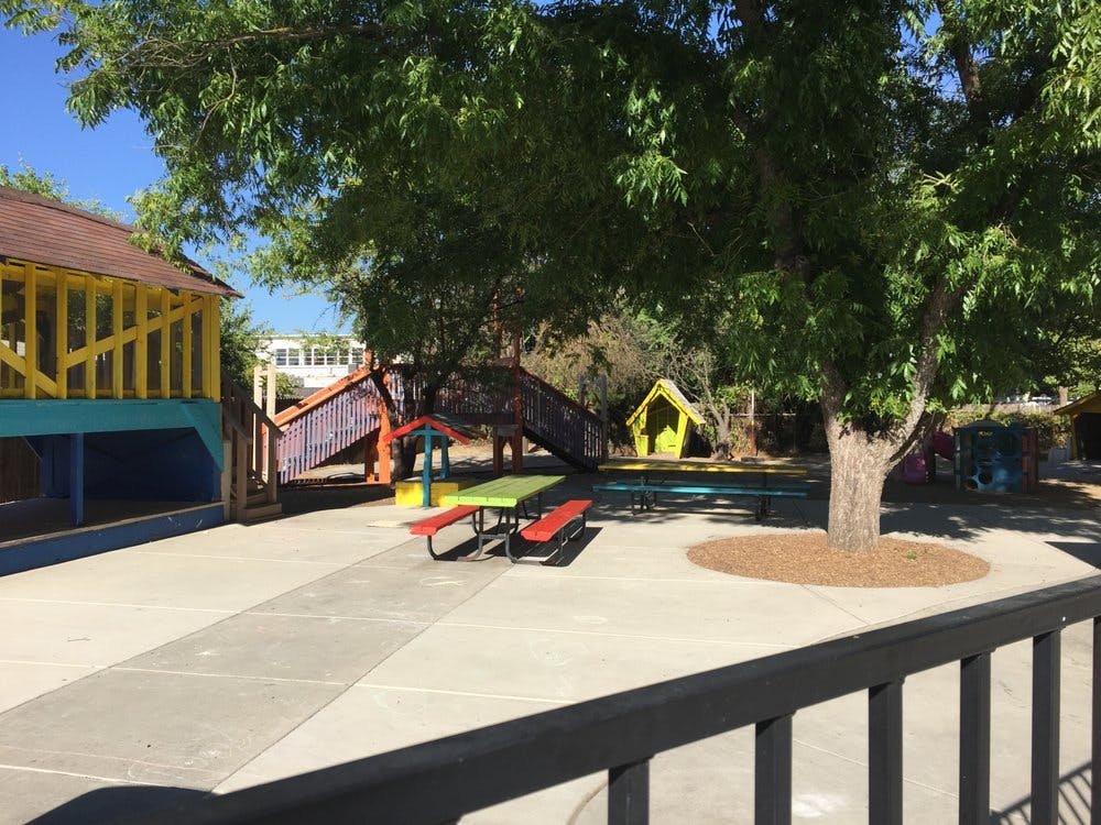 Outdoor playground with colorful structures and a picnic table under a tree