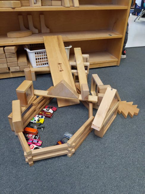Wooden blocks arranged on a carpeted floor with toy cars inside