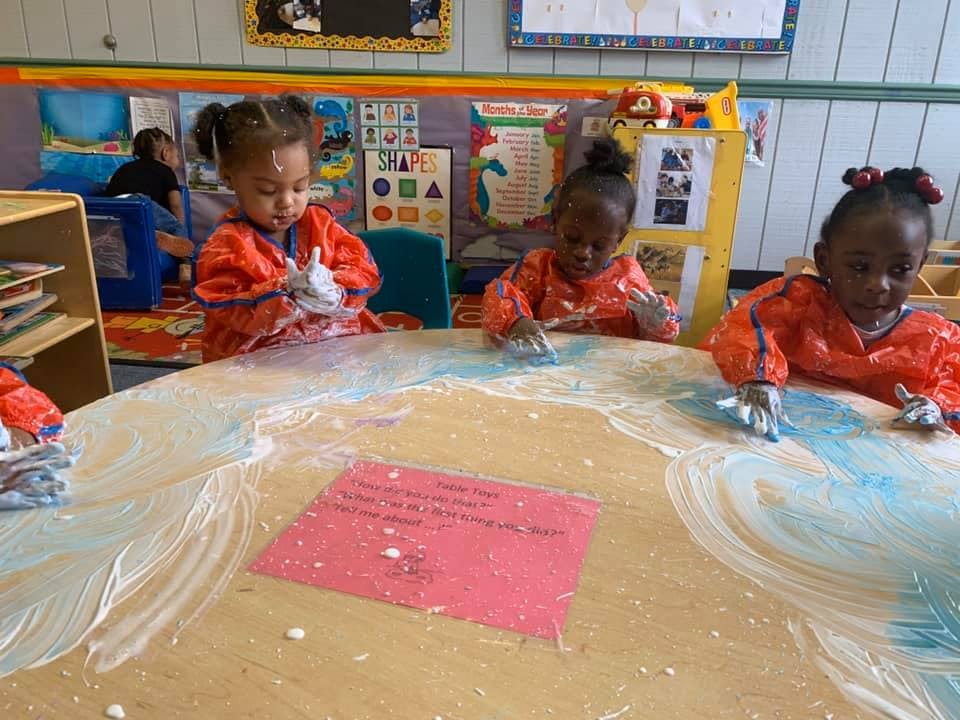 Three children in smocks playing with paint on a table in a classroom