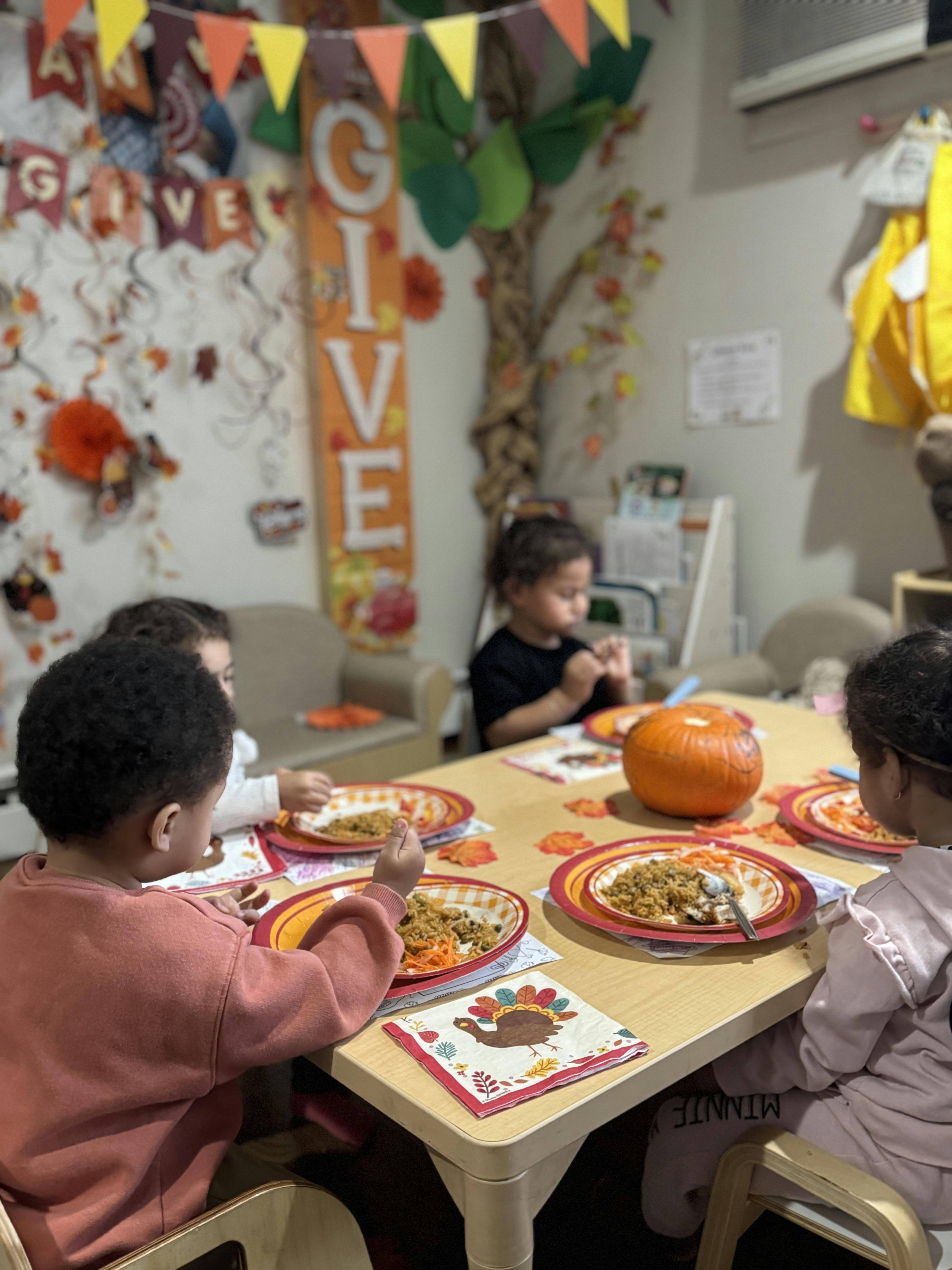 Children sitting around a table with plates of food and a small pumpkin