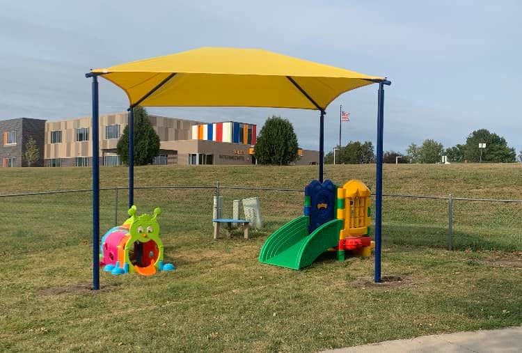 Playground with yellow shade structure, green slide, and caterpillar toy