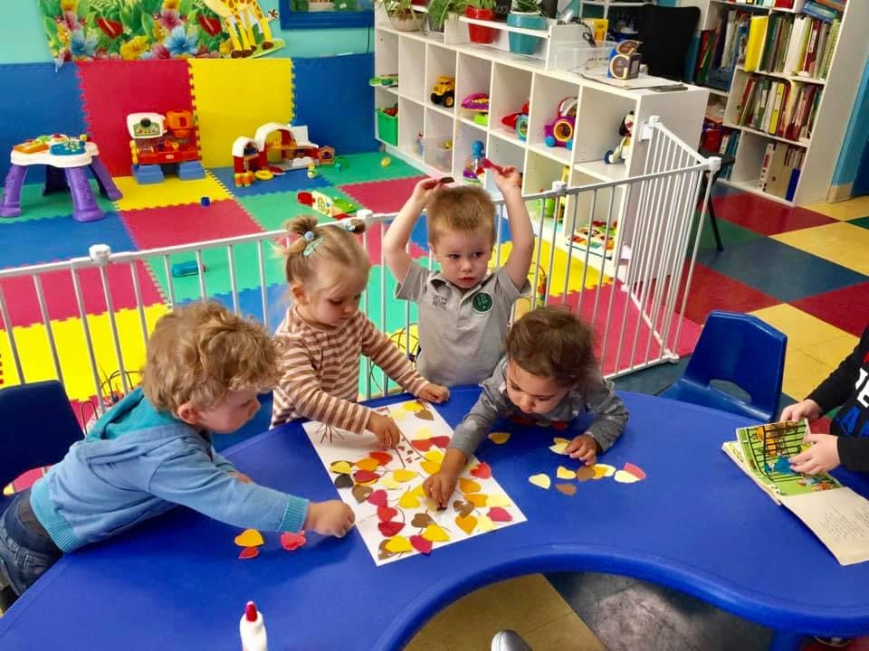 Children playing with colorful shapes at a table in a classroom