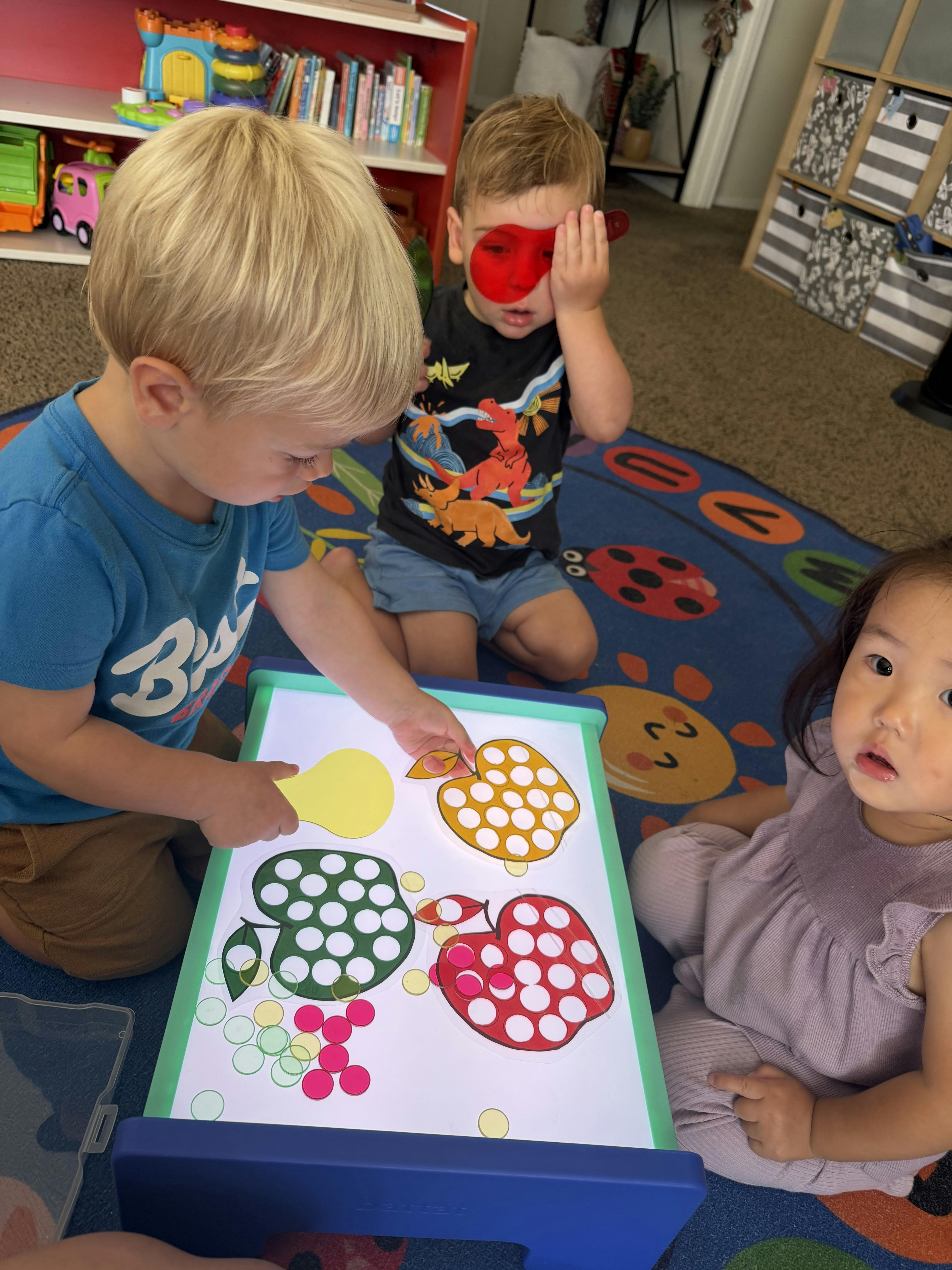 Three children playing with colorful shapes on a light table