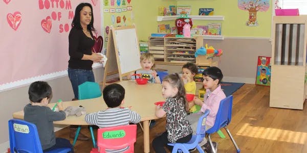 Adult person standing near a table with multiple children seated around it in a classroom