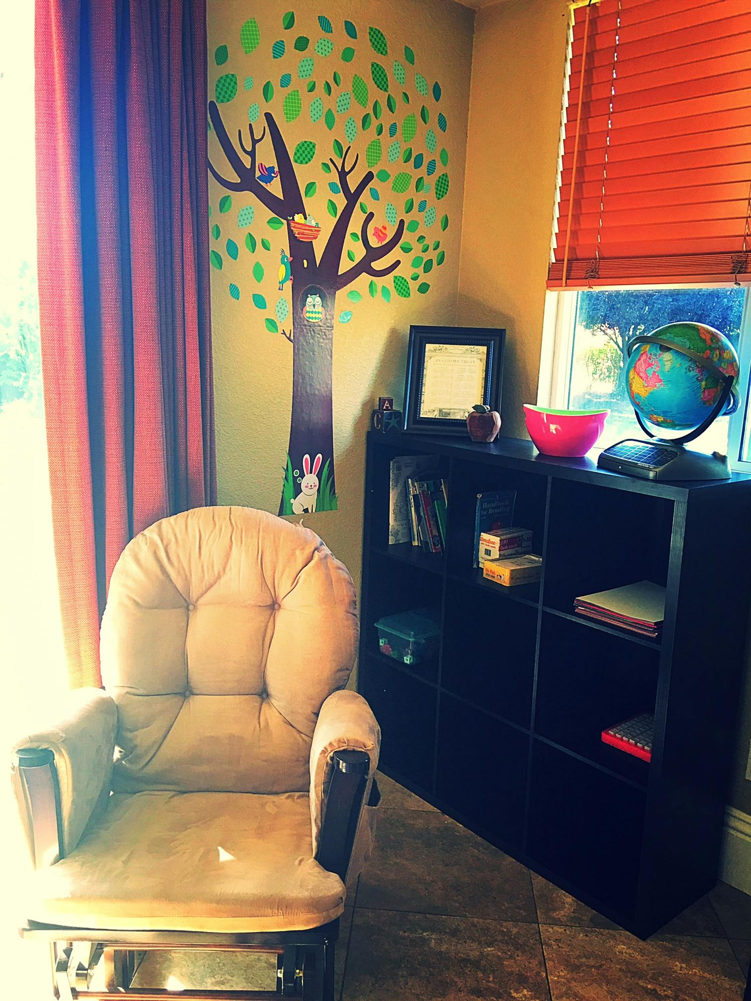 Nursery room with a tree mural, glider chair, and bookshelf
