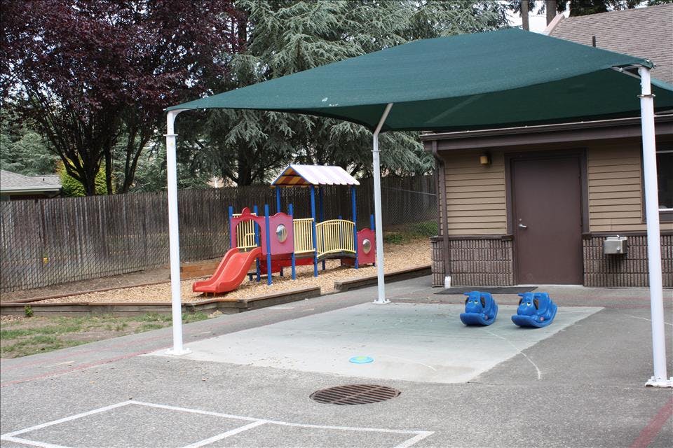 Playground with a small structure, slide, two blue ride-on toys, and a shade cover